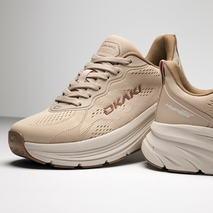 Beige DKNY løpesko med nettingmateriale, tykk hvit såle og brun logo på siden. Sportslig og moderne design.