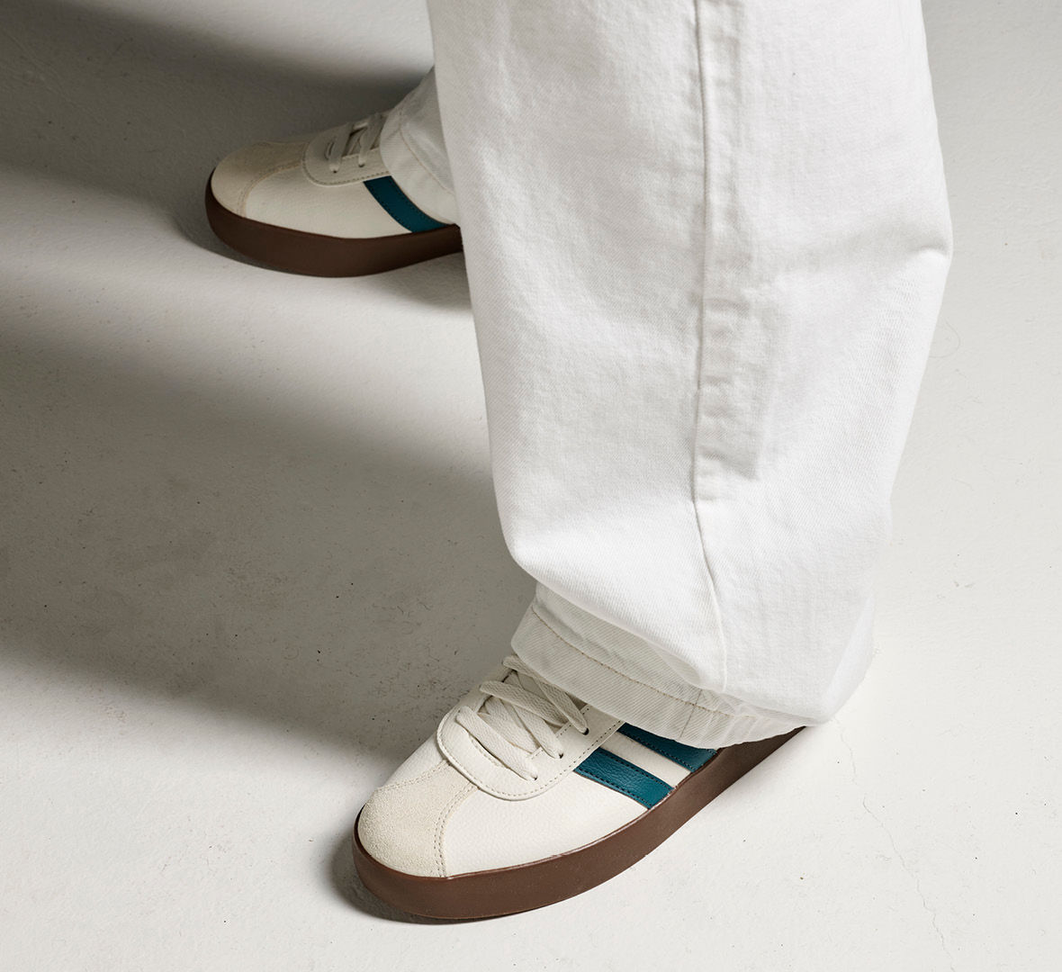 Hvite sneakers med grønne striper og gummisåle, brukt med hvite bukser på lys bakgrunn.