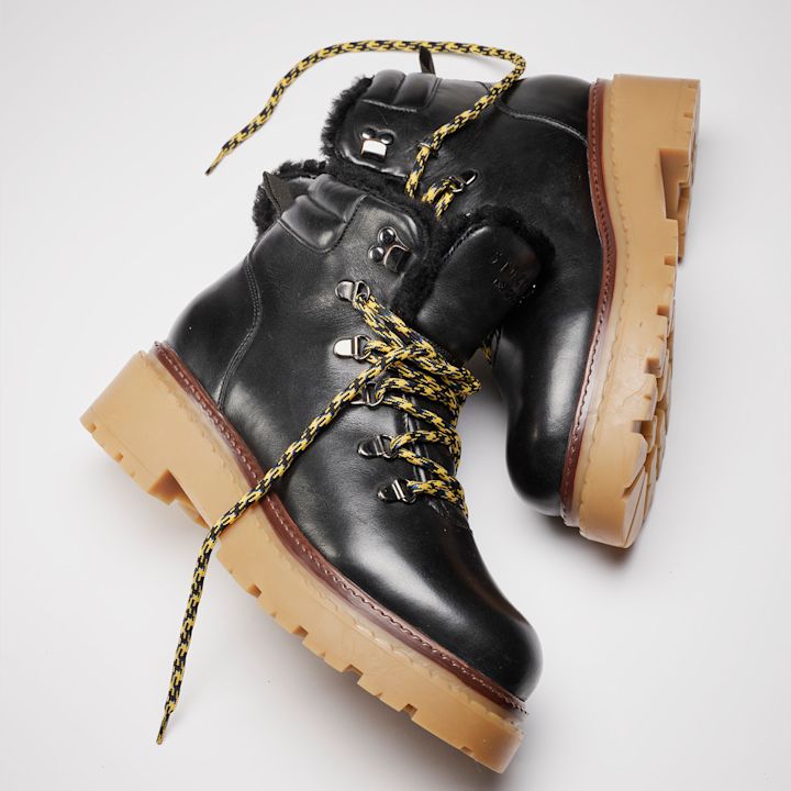 Svarte lærstøvler med pelsfôr, gule og svarte lisser, og beige gummisåle i robust fjellstil.