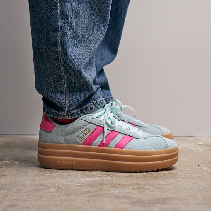 Lyseblå Adidas-sneakers med rosa striper og tykk brun såle, båret med blå jeans på betonggulv.
