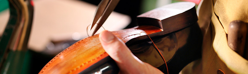 Hånd syr lær på en brun skinnsko med en nål og tråd i et verkstedmiljø.