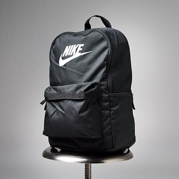 Svart Nike-ryggsekk med hvit logo plassert på en metallkrakk mot grå bakgrunn.