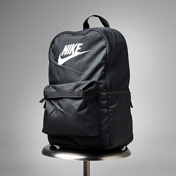 Svart Nike-ryggsekk med hvit logo plassert på en metallkrakk mot grå bakgrunn.