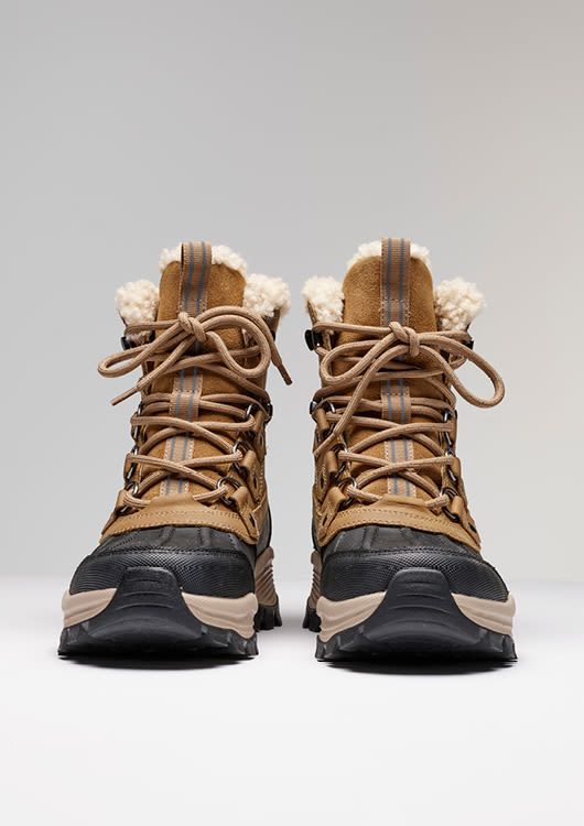 Brune vinterstøvler med pelsfôr, svarte gummisåler og snøring, designet for utendørs bruk i kaldt vær.