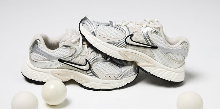 Hvite og sølvfargede Nike løpesko i retrostil med nettingmateriale og svarte detaljer, plassert bak tre hvite julekuler.