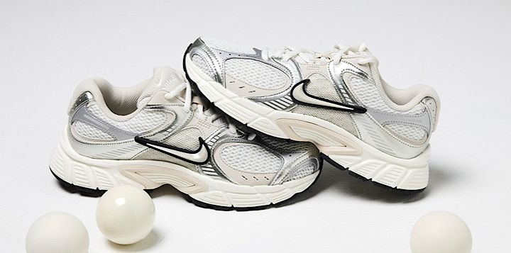 Hvite og sølvfargede Nike løpesko i retrostil med nettingmateriale og svarte detaljer, plassert bak tre hvite julekuler.