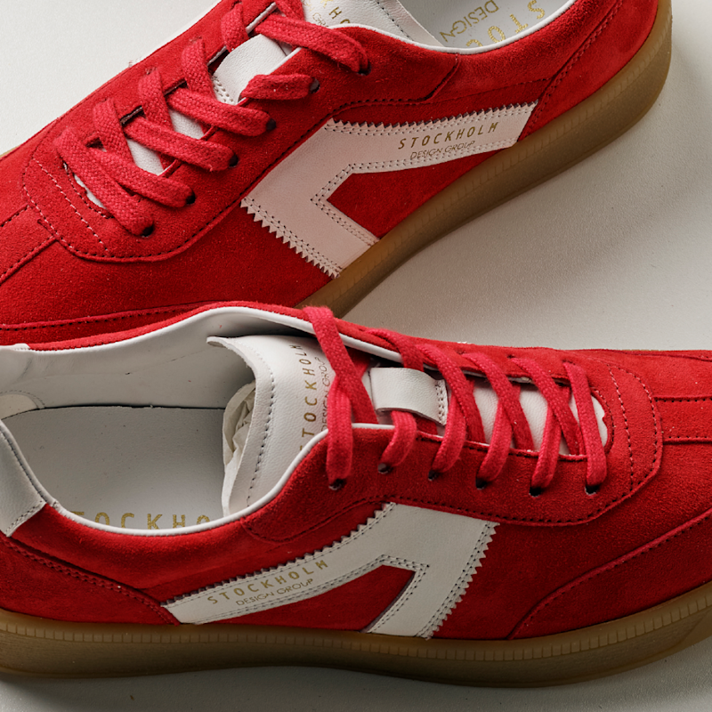 Røde sneakers i semsket skinn med hvite detaljer og brune såler, merket "Stockholm Design Group", plassert på hvit bakgrunn.