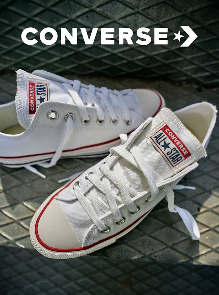 Hvite Converse Chuck Taylor All Star lavskaftede canvas-sneakers med røde detaljer og hvite snørebånd.