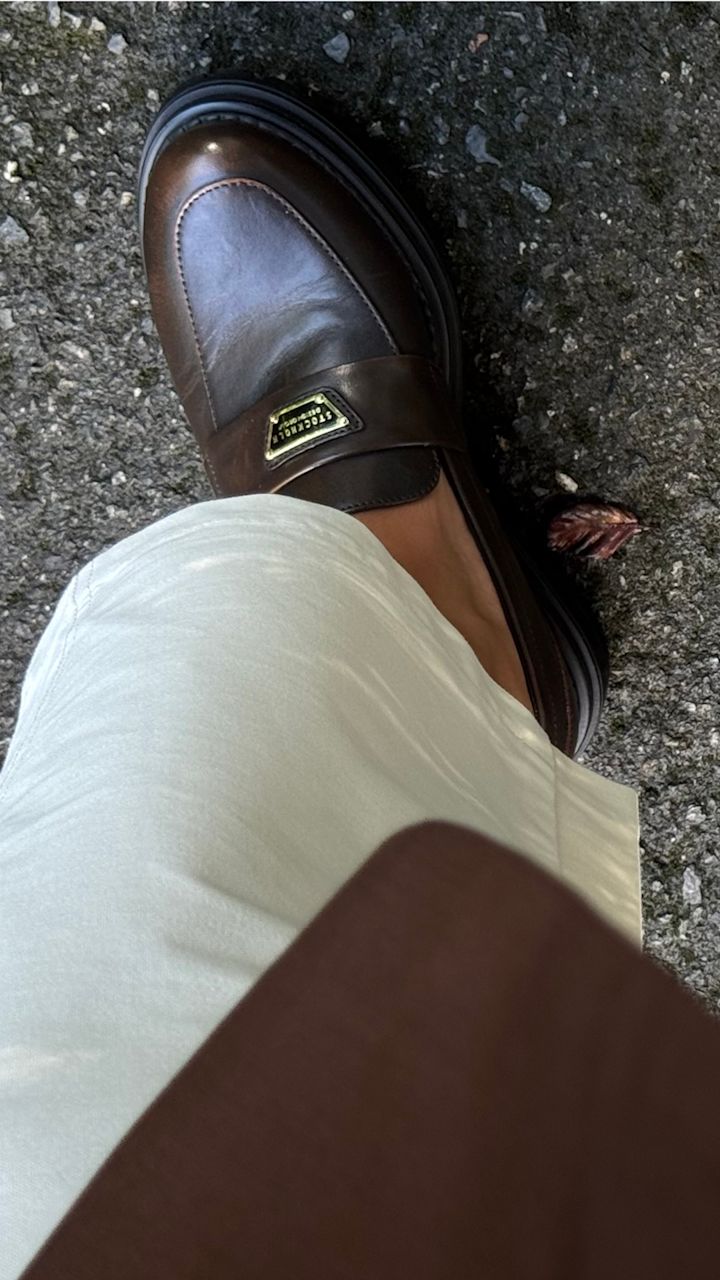 Brune skinnloafers fra Stockholm Design Group med metalldetalj og tykk såle, sett ovenfra mot asfalt, kombinert med hvitt plagg.