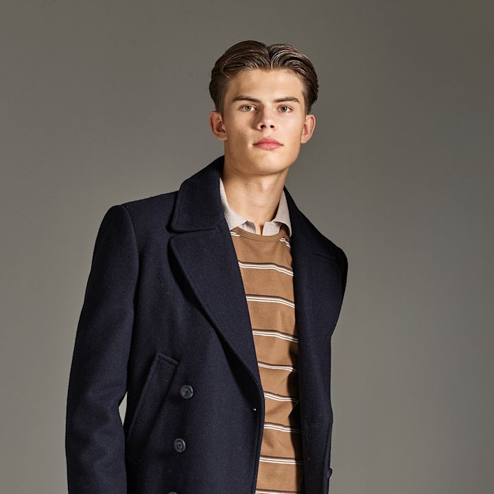 PeGuttrson i mørkeblå ullkåpe over brun stripete genser mot nøytral bakgrunn.