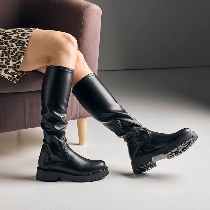 høye elastiske støvletter på modell med bare bein. modell sitter i en sofastol med kort leopardskjørt.