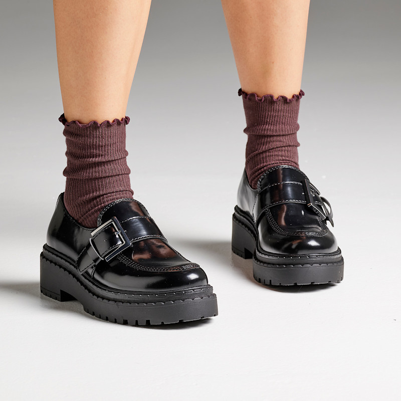 Svarte, blanke loafers med spenne og kraftig såle, kombinert med brunaktige sokker med rynkekant.