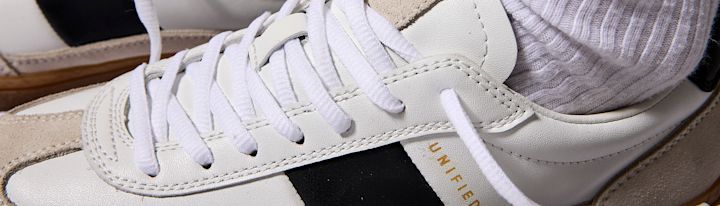 Hvitt og beige skinnsko med hvite lisser og svart detalj, iført hvit ribbestrikket sokk.