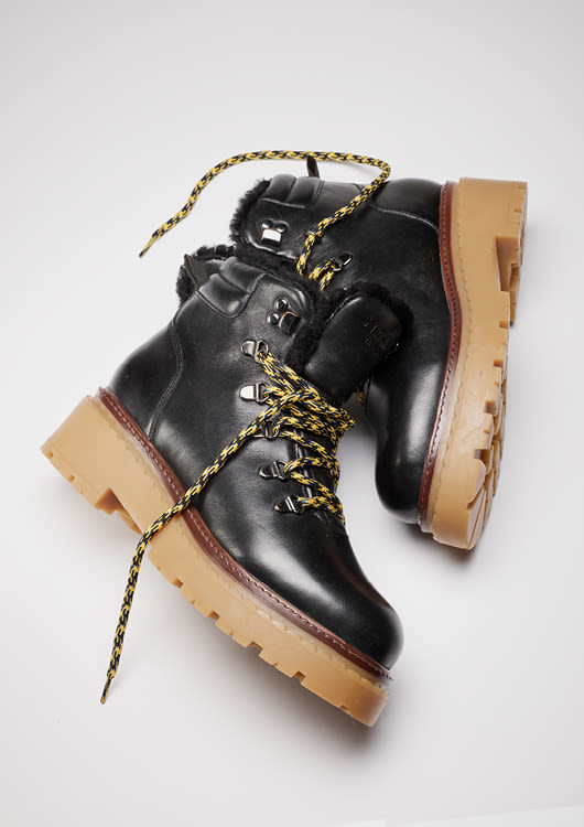 Svarte vinterstøvler med pelsfôr, gule og svarte lisser, og kraftig lysebrun gummisåle på grå bakgrunn.