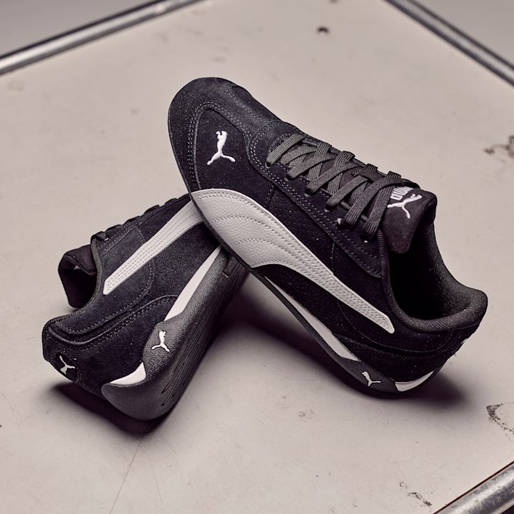 Svarte Puma sportssko med hvite sidedetaljer, plassert på en lys overflate. Klassisk lavprofil design med Puma-logo.