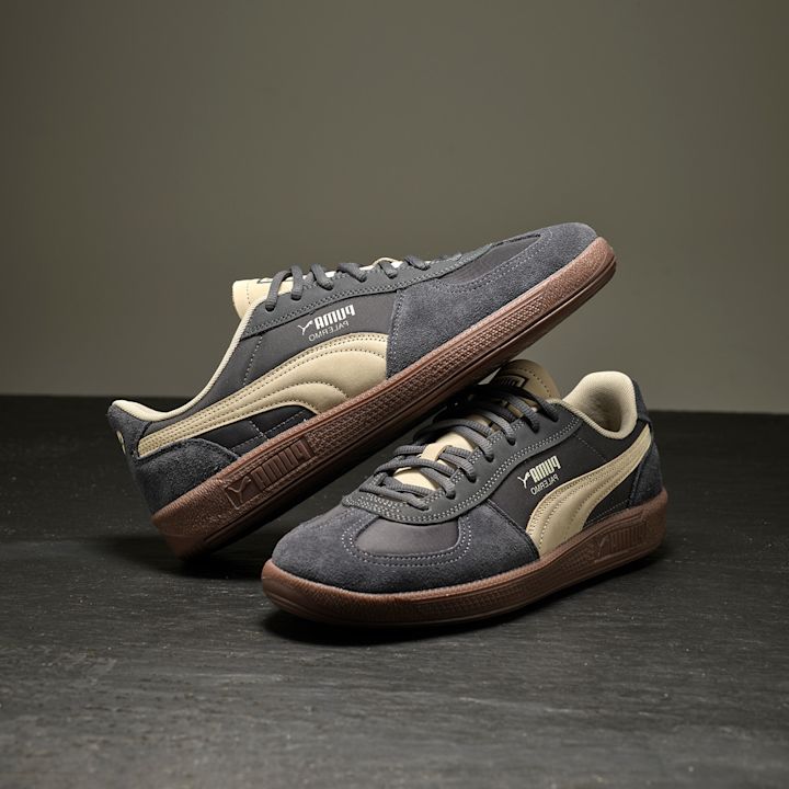 Grå og beige Puma sneakers i retrostil med semsket overflate og brun gummisåle, plassert på mørk overflate.