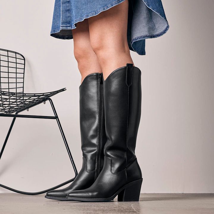 sorte cowboyboots på modell tatt i studio med sort nettingstol i bakgrunnen 