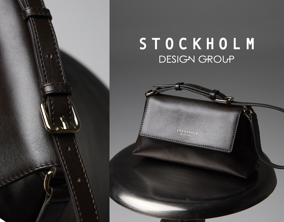 Elegant svart skinnveske fra Stockholm Design Group med gulldetaljer, vist på mørk overflate med logo i bakgrunnen.