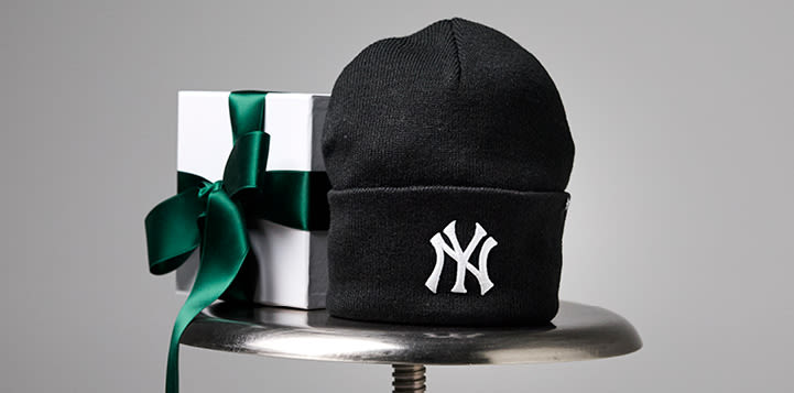 Svart NY Yankees-lue ved siden av en hvit gaveeske med grønn sløyfe, plassert på en metalloverflate.