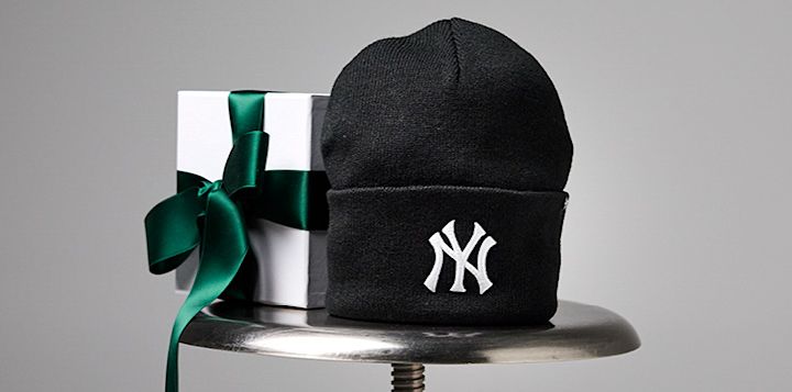 Svart NY Yankees-lue ved siden av en hvit gaveeske med grønn sløyfe, plassert på en metalloverflate.