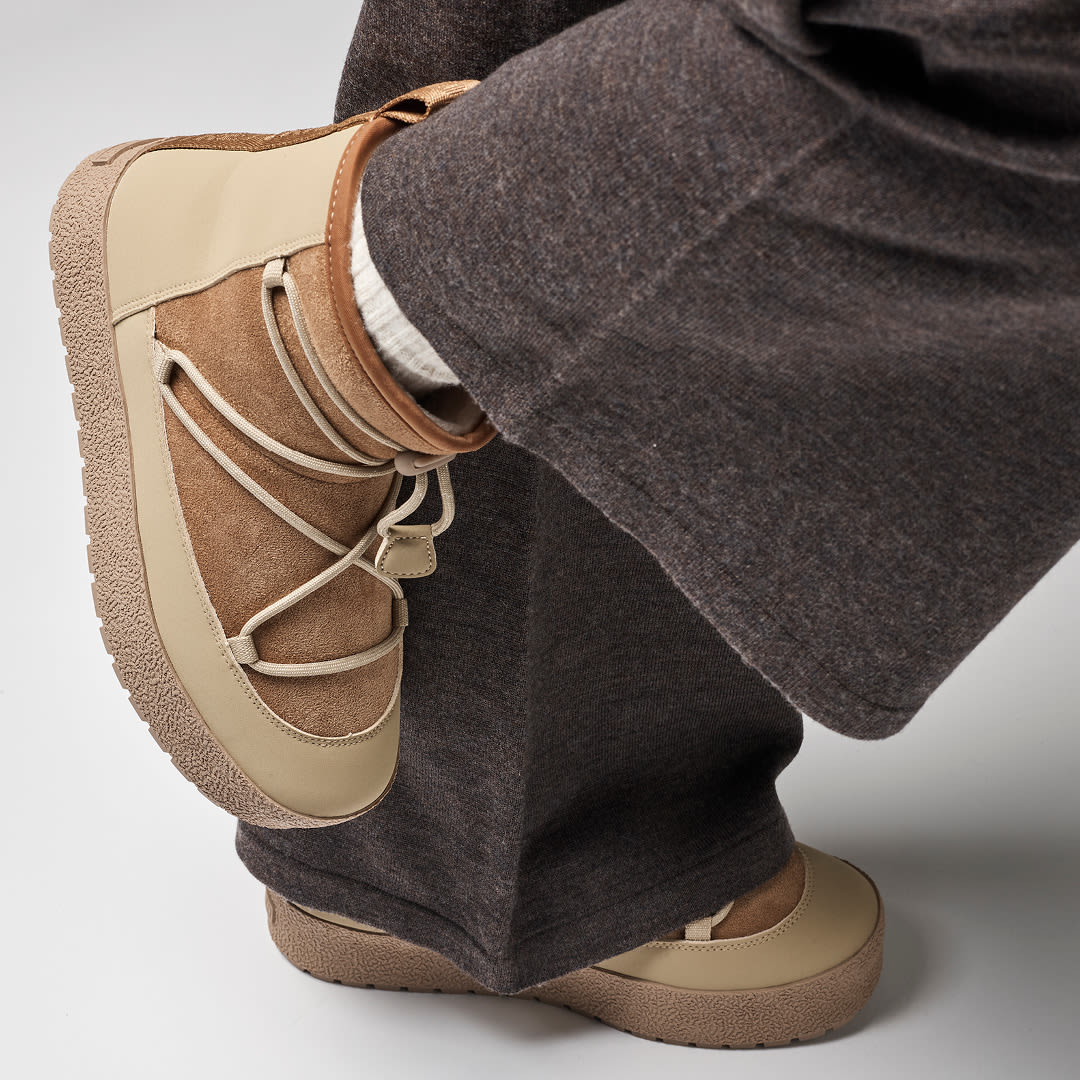 Beige og brune semsket snowboots med snøring og gummisåle, brukt med mørke grå bukser og hvite sokker.