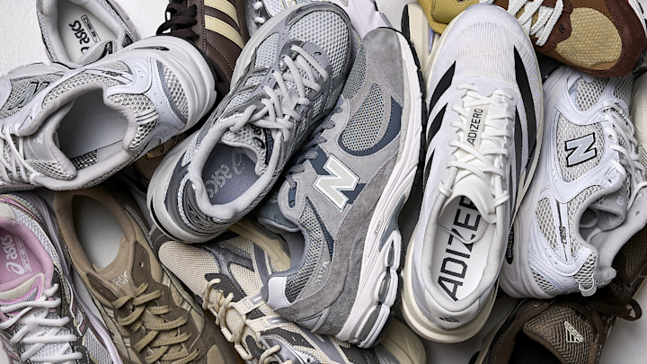 Samling av sneakers fra New Balance, Adidas og Asics i grå, beige, hvit og brun, stablet oppå hverandre.