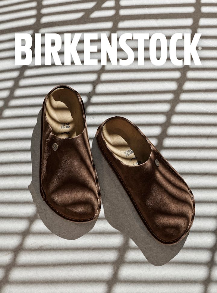 Birkenstock clogs i brun skinn med beige fotseng og lys såle, sett ovenfra i sollys.