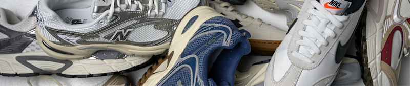 Ulike sneakers i grå, blå og hvit, inkludert New Balance og Nike modeller, plassert ved siden av hverandre.