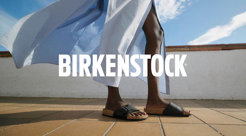 Sorte Birkenstocksandaler på fot på en flislagt balkong med flagrende lys kjole