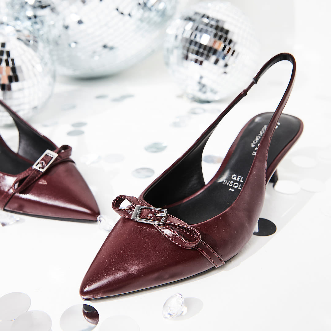 Elegante vinrøde slingback-pumps med spiss tå, sløyfedetalj og stiletthæl, omgitt av diskokuler og pyntedekorasjoner.