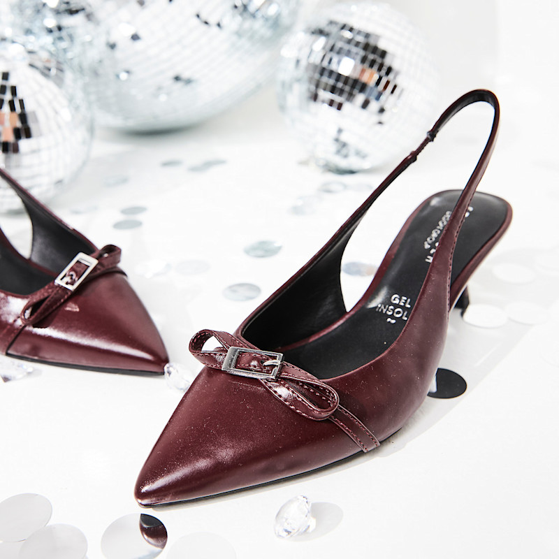 Elegante vinrøde slingback-pumps med spiss tå, sløyfedetalj og stiletthæl, omgitt av diskokuler og pyntedekorasjoner.