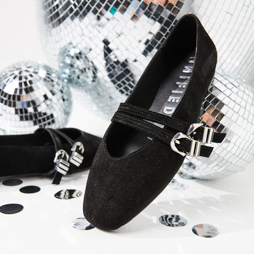 Svarte semsket ballerinasko med sølvspenne fra UNITED, fotografert mot diskokuler i bakgrunnen for et festlig preg.