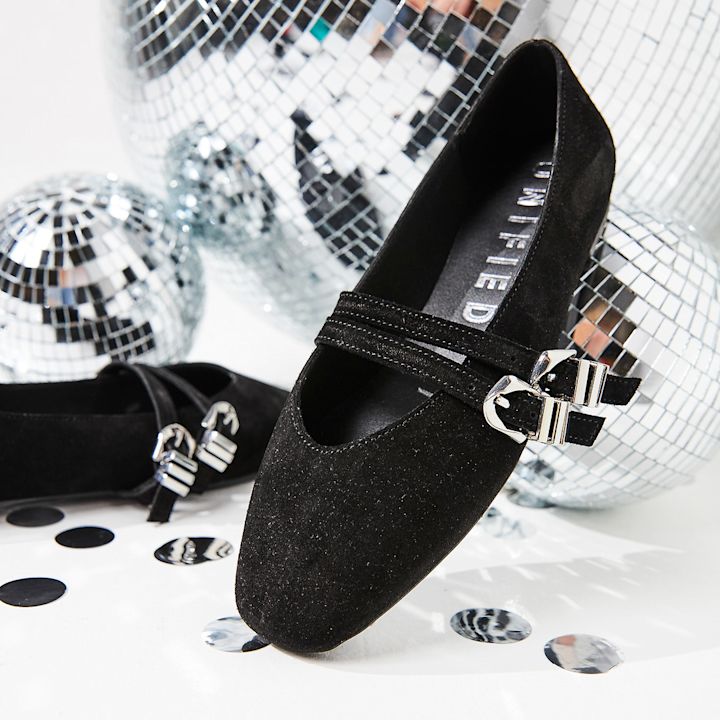 Svarte semsket ballerinasko med sølvspenne fra UNITED, fotografert mot diskokuler i bakgrunnen for et festlig preg.