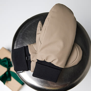 Beige vannavvisende votter plassert på en metallisk rund overflate, med en pakke med grønn sløyfe i bakgrunnen.