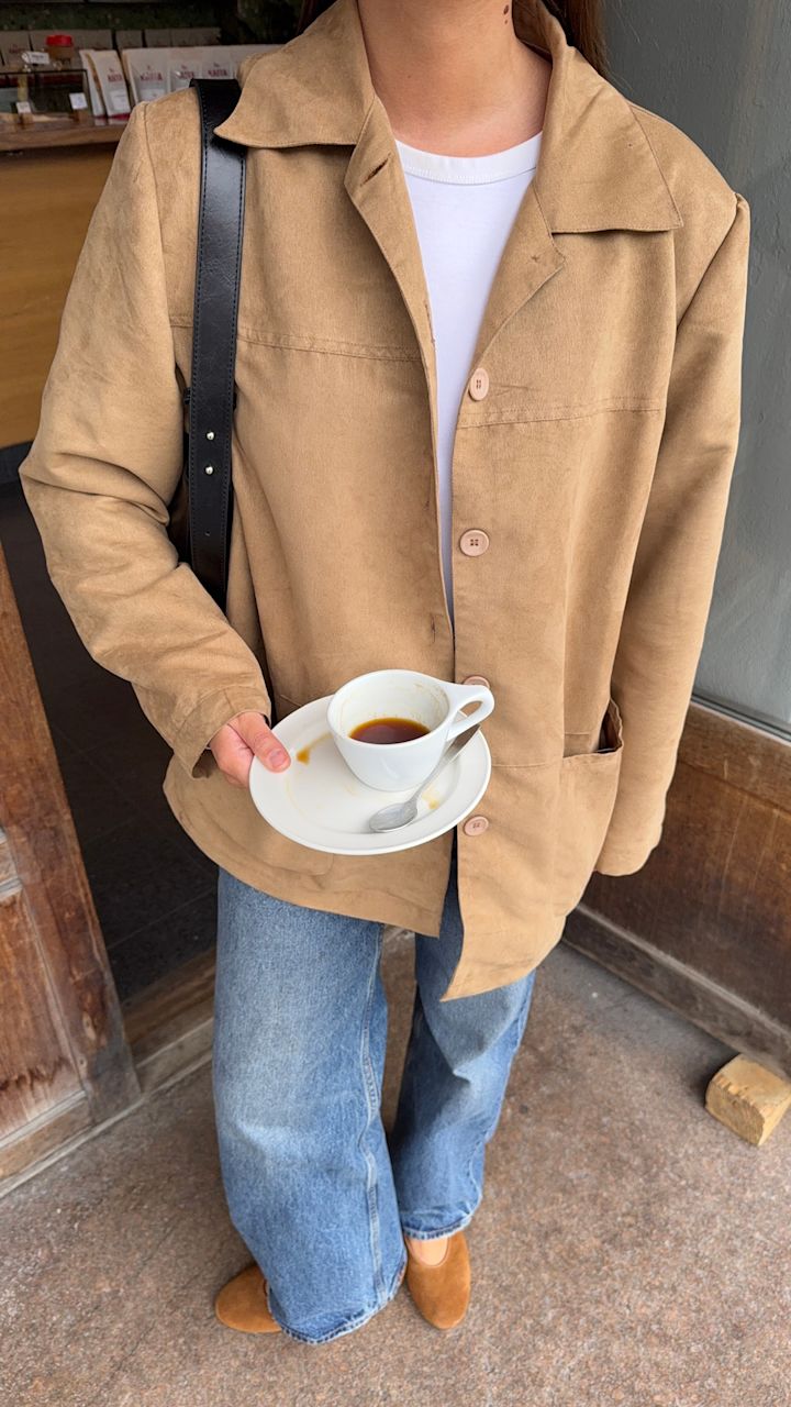 Lisa Alexandra i beige jakke og jeans holder kaffekopp, med lysebrune semsket ballerinasko fra Unified på føttene.