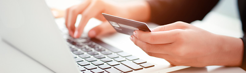 Hender holder et kredittkort og taster på et laptop-tastatur i et lyst miljø.