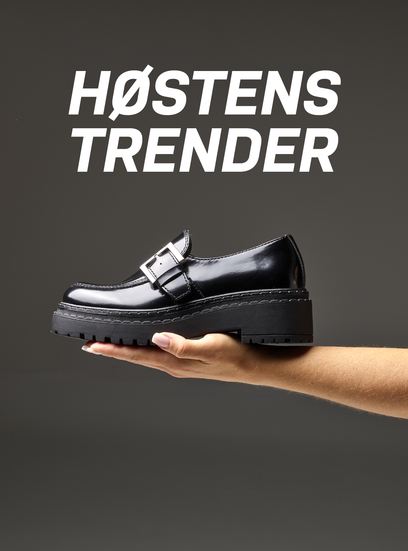 Hånd holder blank svart loafer med spenne og kraftig platåsåle. Teksten "HØSTENS TRENDER" vises over skoen.