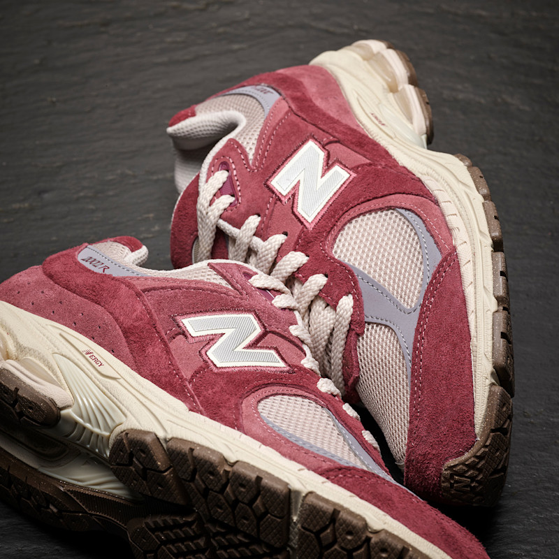 Vinrøde New Balance sneakers med semsket skinn og hvite detaljer, plassert på mørk overflate.