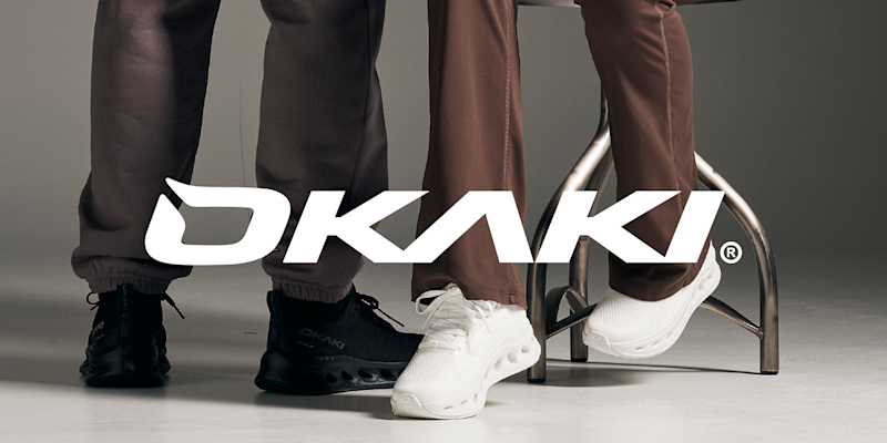 Logo: OKAKI over to personer som står og sitter med svarte og hvite joggesko på grått gulv.