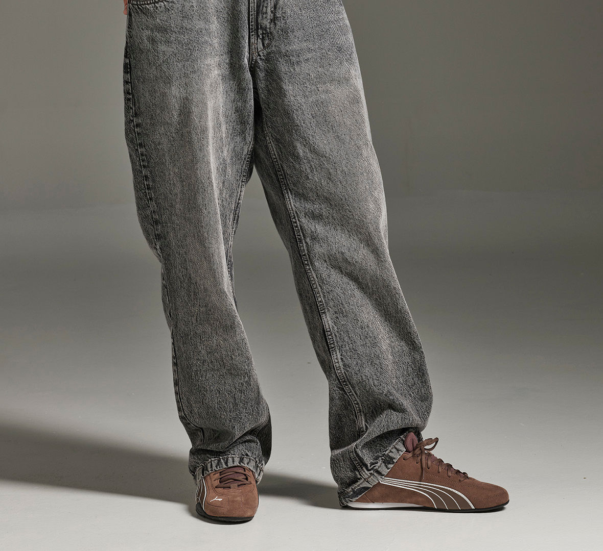 Grå jeans med brune sportssko fra PUMA i semsket skinn med hvite striper på siden, i casual stil.