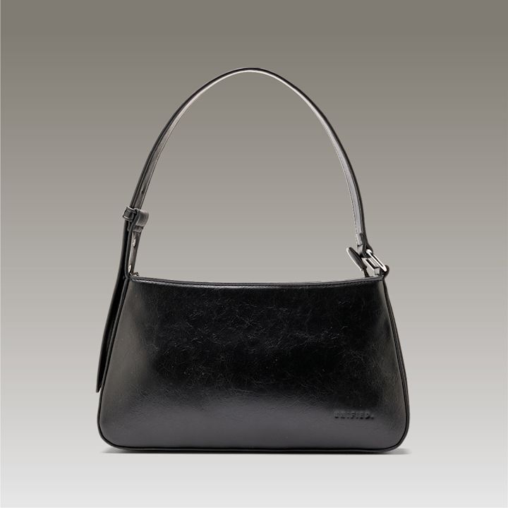 Elegant svart veske med smalt håndtak og metalldetaljer, fotografert mot nøytral grå bakgrunn.