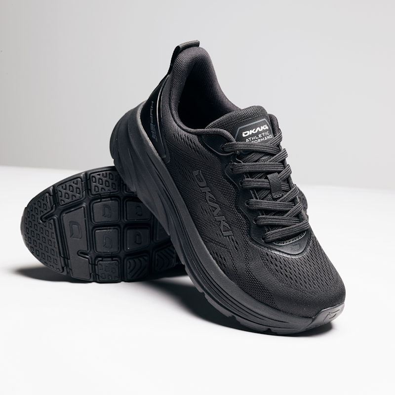 Svart løpesko med merkene "DKAKI" og "Athletic Performance" plassert på en hvit overflate, med en sko liggende på siden som viser sålen.