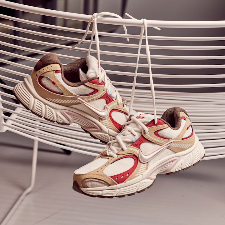 Nike sneakers i beige, hvit og rød - hengende fra hvit metallstol med lissene knyttet sammen.